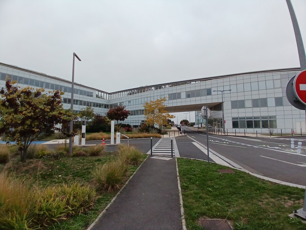 View of a modern glass building with landscaped surroundings, including trees and a pathway.